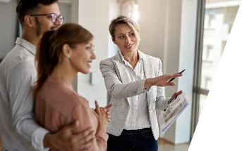 Un agente inmobiliario sonriente habla con una pareja interesada en comprar una casa nueva-peritavalue